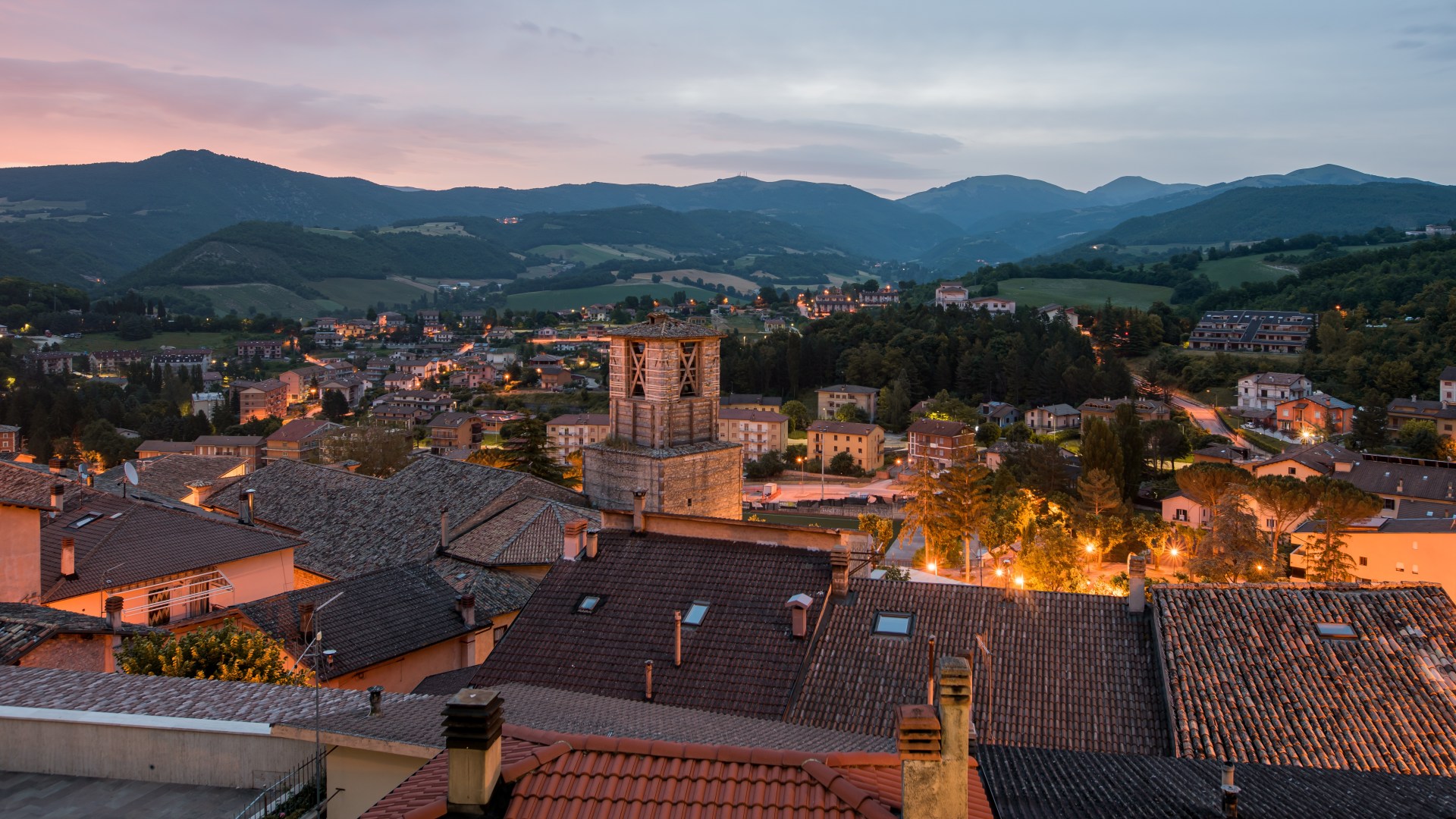 High angle shot of a lot of buildings with lights surrounded by green trees in Cascia, Italy